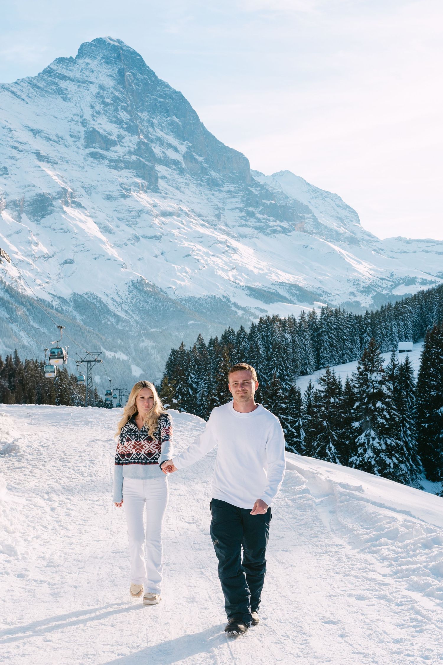 A couple dances joyfully in an alpine meadow with snow-capped mountain peaks creating a majestic backdrop.