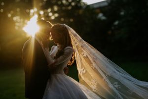 Golden hour wedding portraits with sunflare through flowing veil.