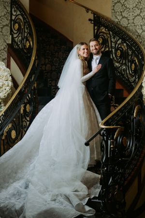 Wedding portrait on grand spiral staircase with ornate iron railings and flowing white dress.