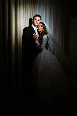 A bride and groom pose together in a dark hallway with dramatic lighting creating a moody wedding portrait.