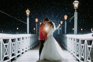Romantic nighttime wedding photo on illuminated white bridge with falling snow.