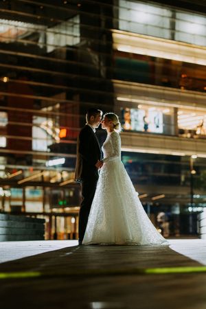Silhouetted bride and groom share an intimate moment in a modern industrial venue with dramatic lighting.