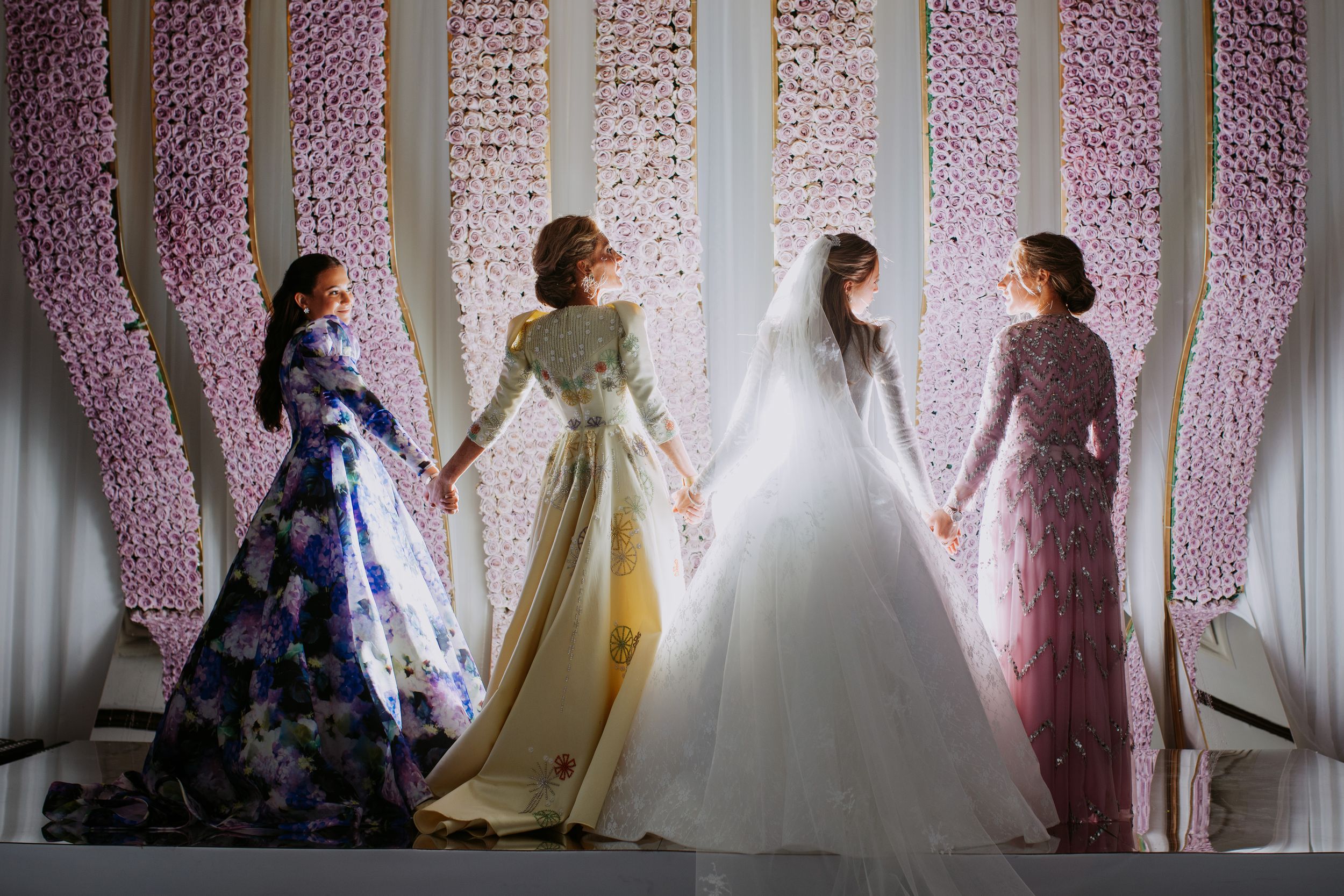 A row of elegant white wedding dresses on display against a pink floral backdrop in a bridal boutique.