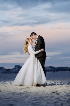 Romantic beach wedding portrait at sunset with cloudy sky backdrop.