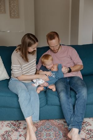 Family shares intimate moment together on teal sofa with patterned rug below.