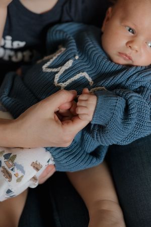 Baby wearing blue knit sweater lies peacefully during indoor photo session.