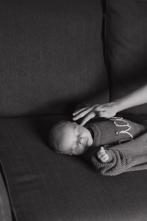 A sleeping baby lies peacefully on a dark couch in a black and white photo series.