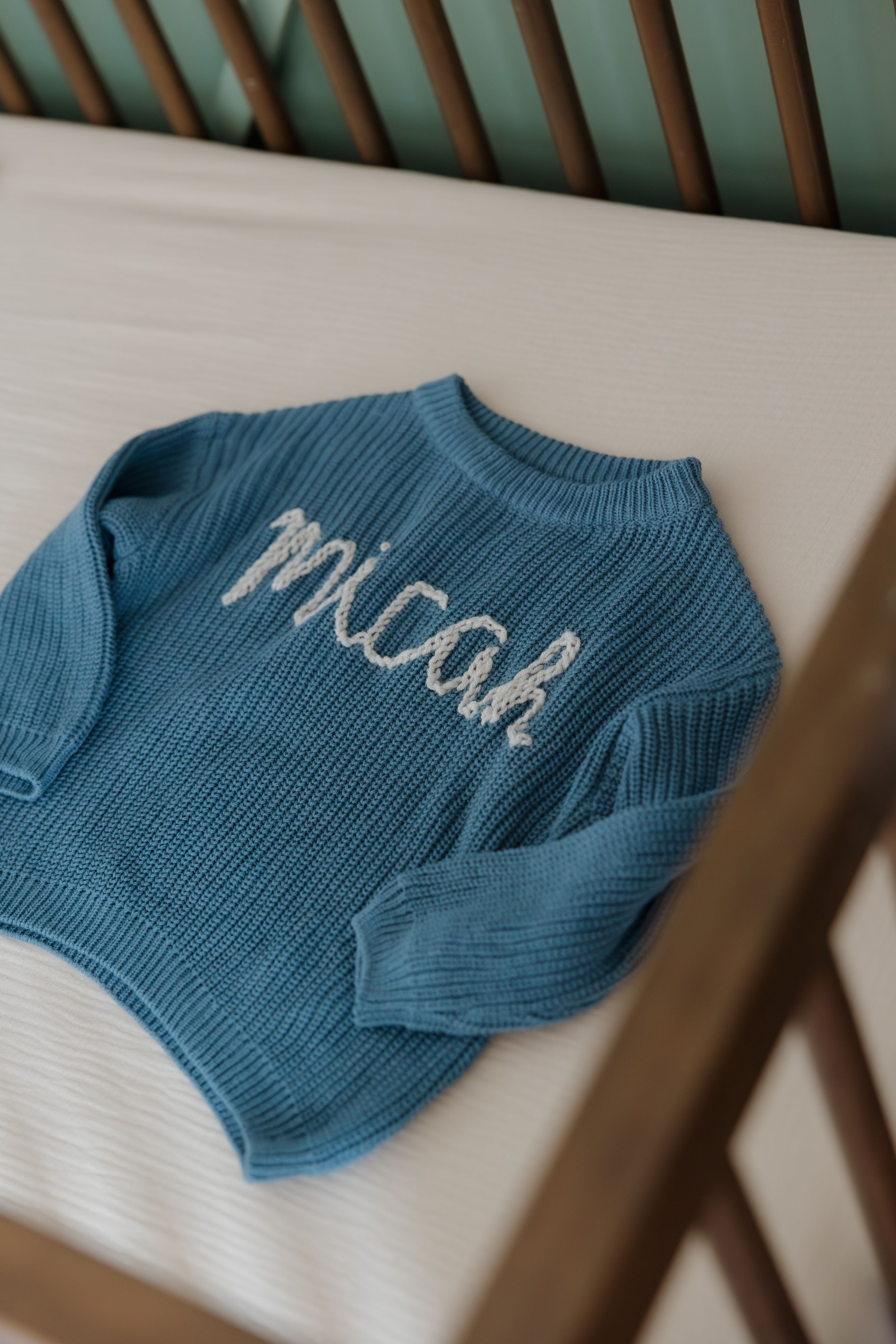 A blue knit sweater with text embroidery lying on a white surface.