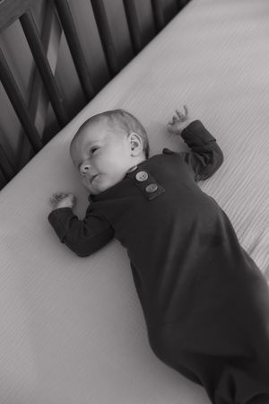 Black and white photos of a sleeping baby in dark clothing on a crib mattress.