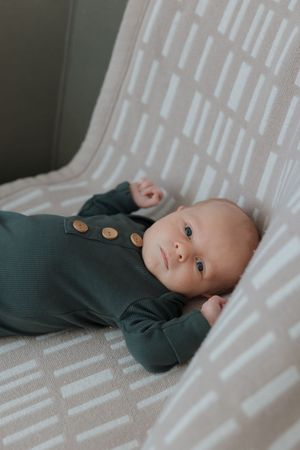 A baby in dark clothing lying on a white textured surface looking at the camera.