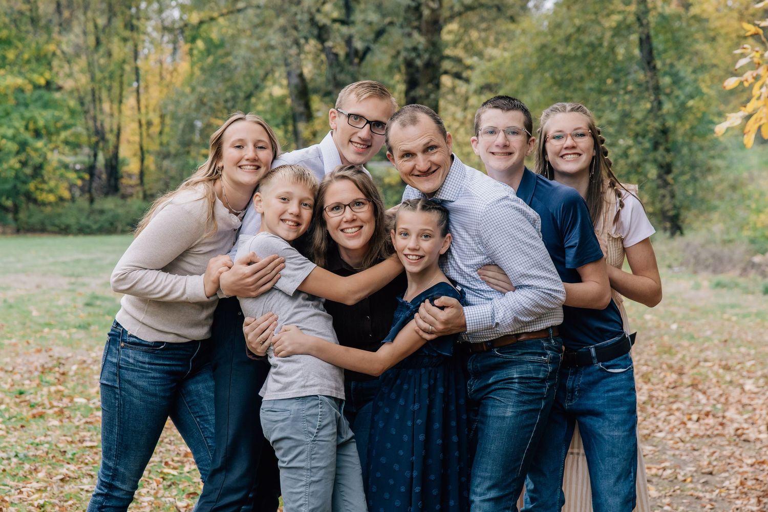Joyful family of eight hugging and smiling together in a colorful fall park.
