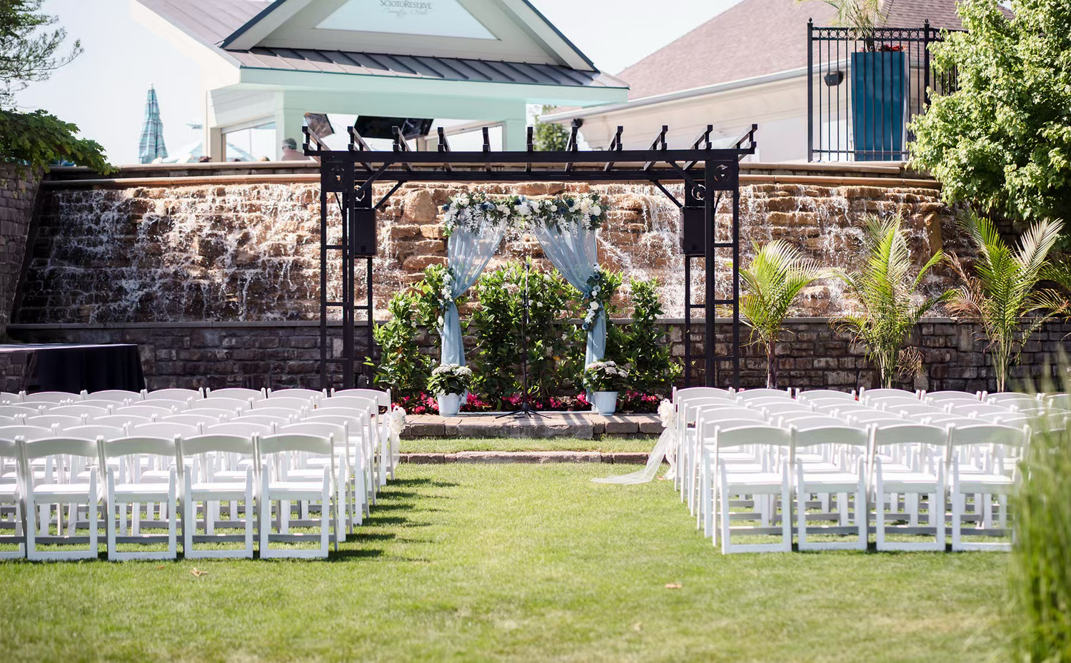 White folding chairs arranged in rows on a lush green lawn for an outdoor wedding ceremony with stone walls for Columbus Ohio wedding venues