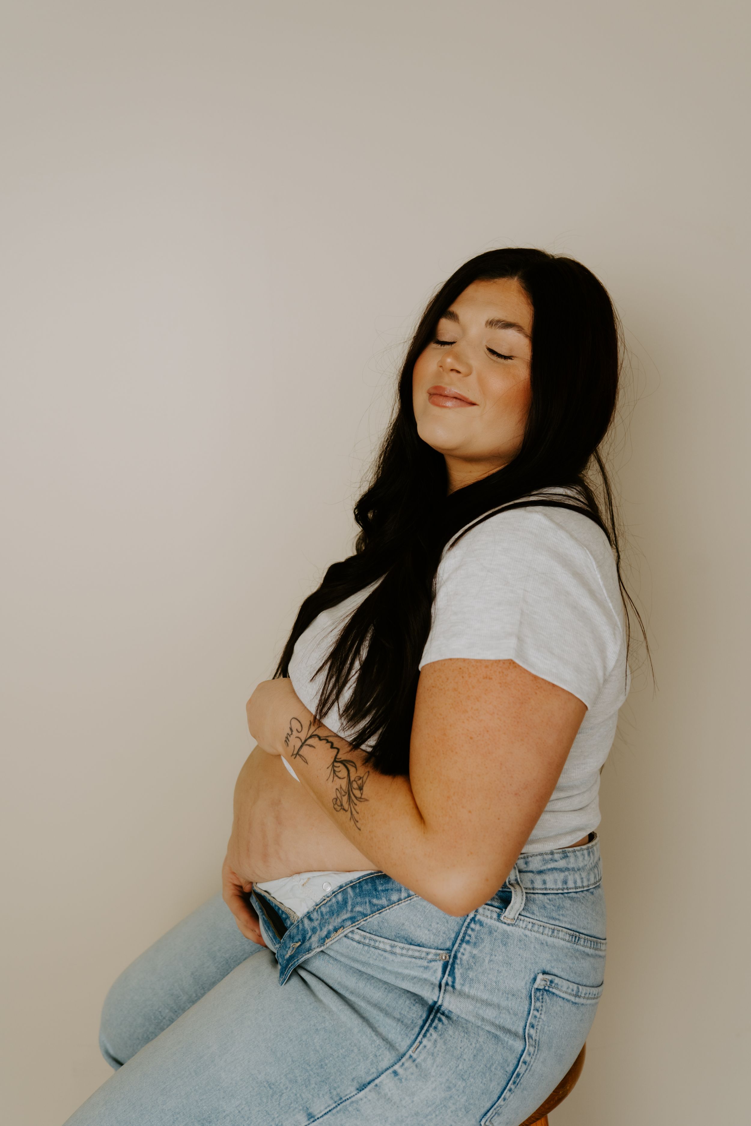 A woman in denim and t-shirt poses confidently on a wooden stool.