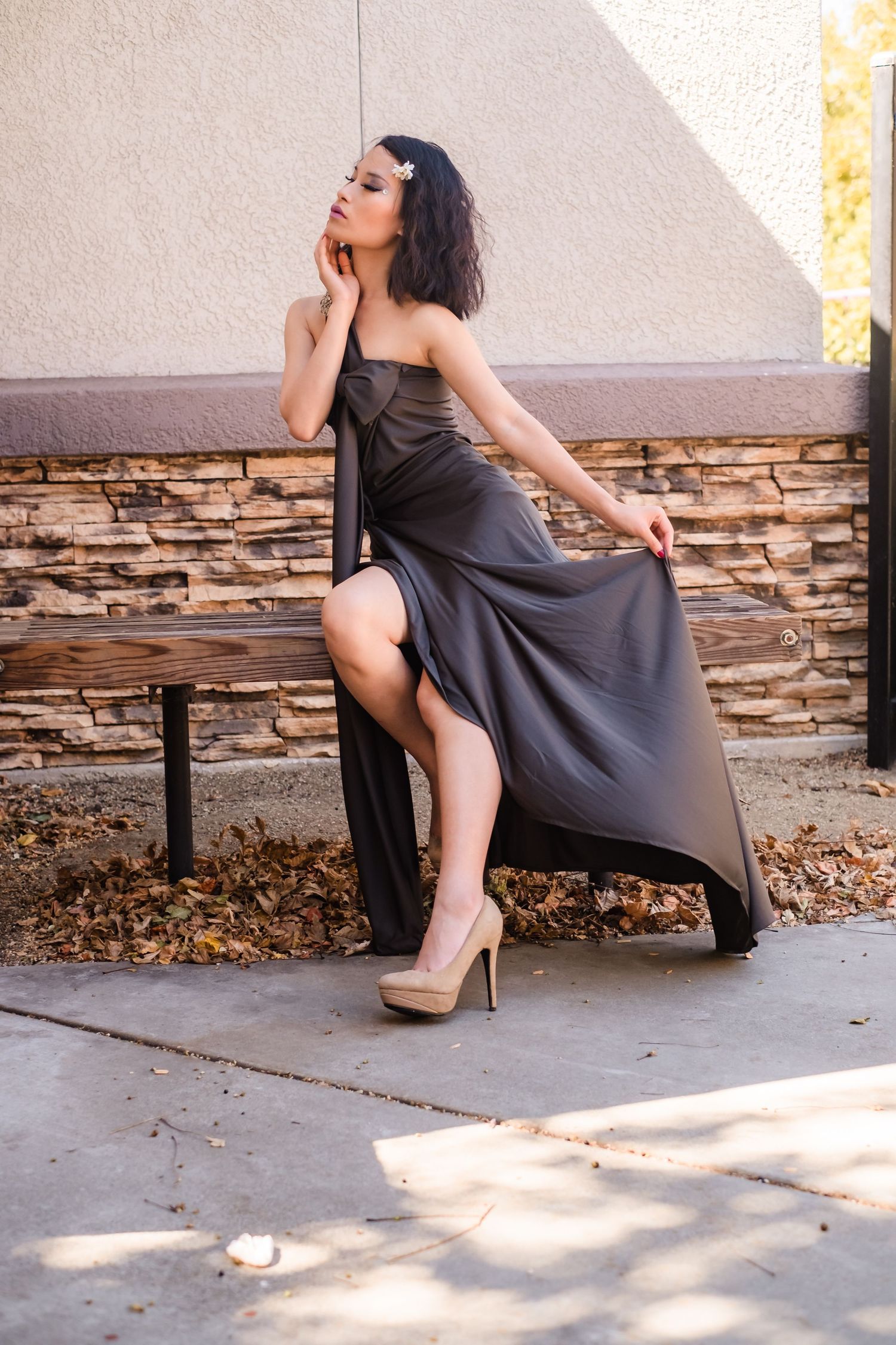 A model in a gray dress poses dramatically on a stone bench against a textured wall. Before taking the runway in Vacaville California