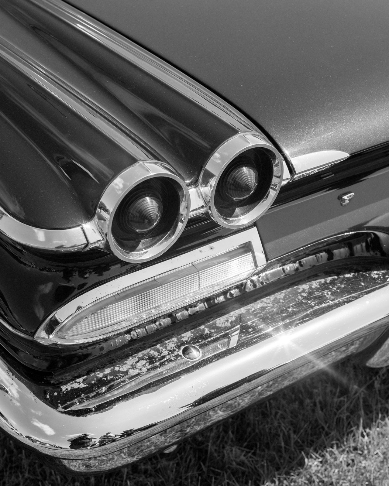 Close-up black and white detail of classic car tail lights and chrome trim showing iconic 1950s automotive styling.