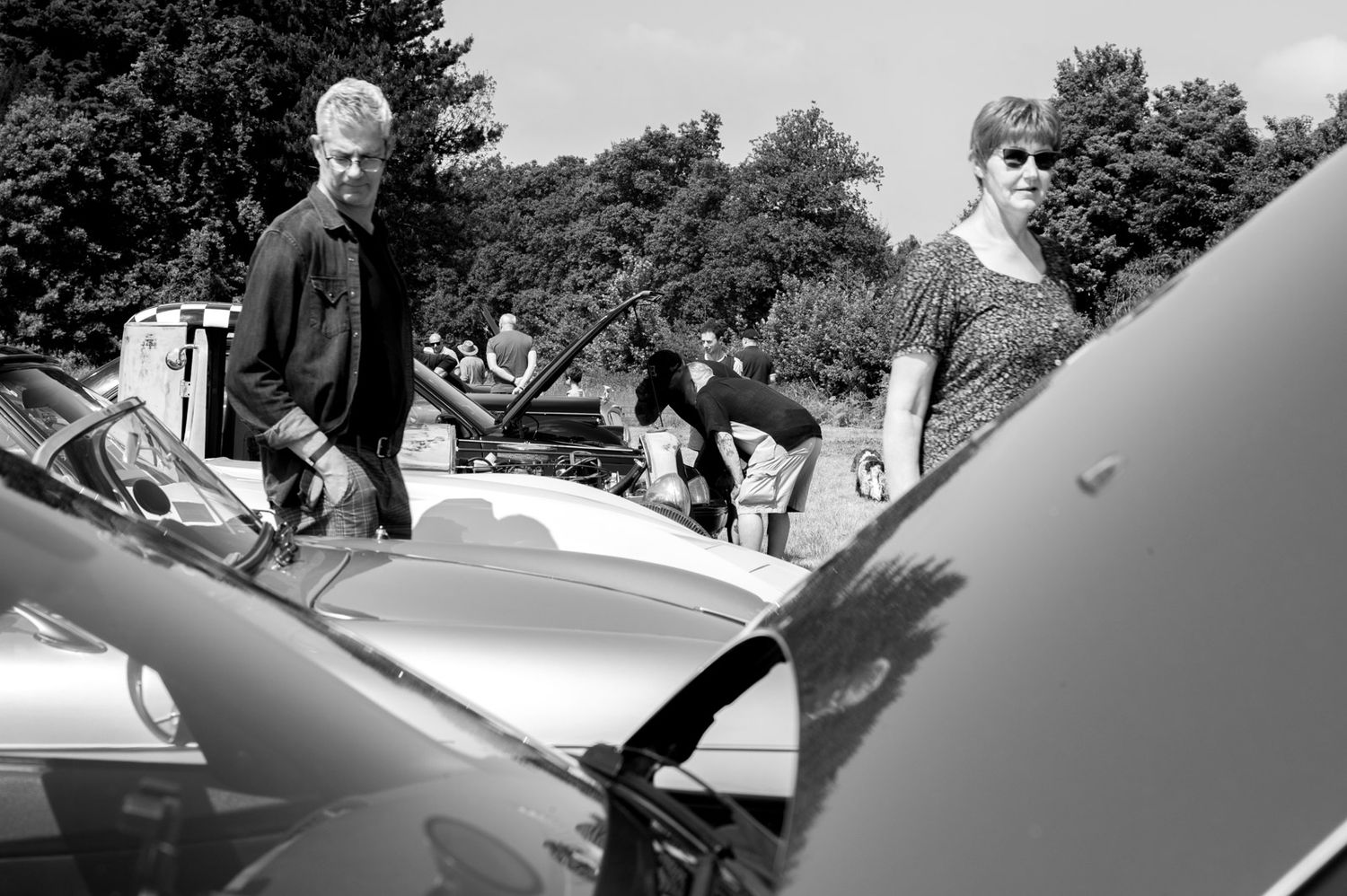 Black and white photo of people gathered around vintage cars at an outdoor car show.