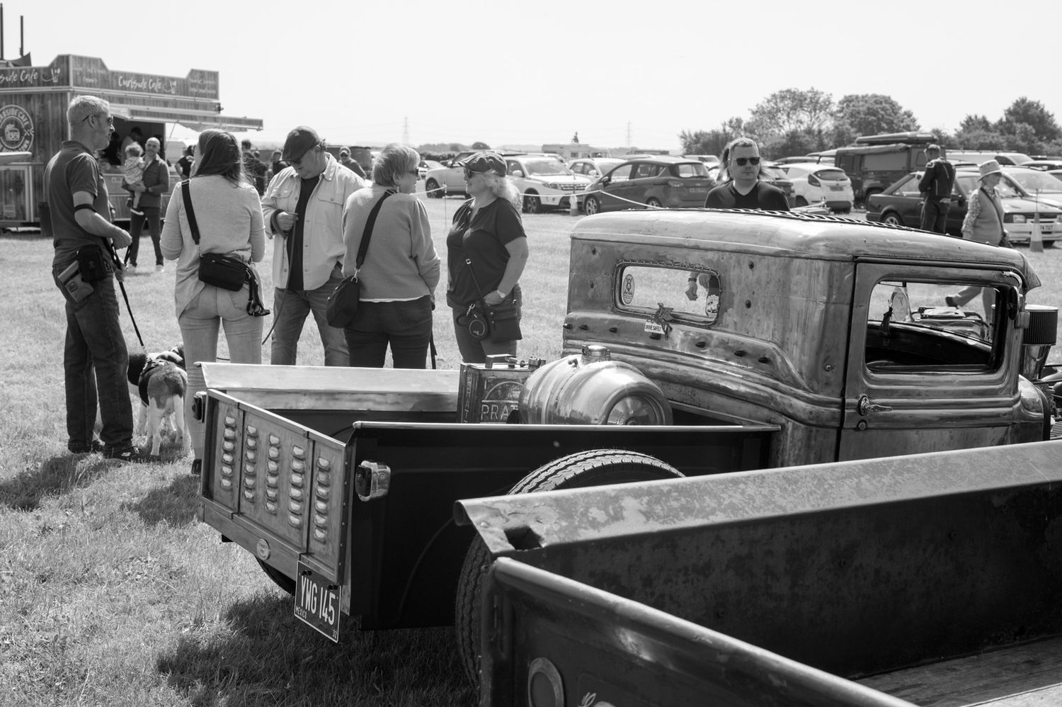 A vintage black and white photograph shows a group of classic cars lined up at an outdoor event or gathering.