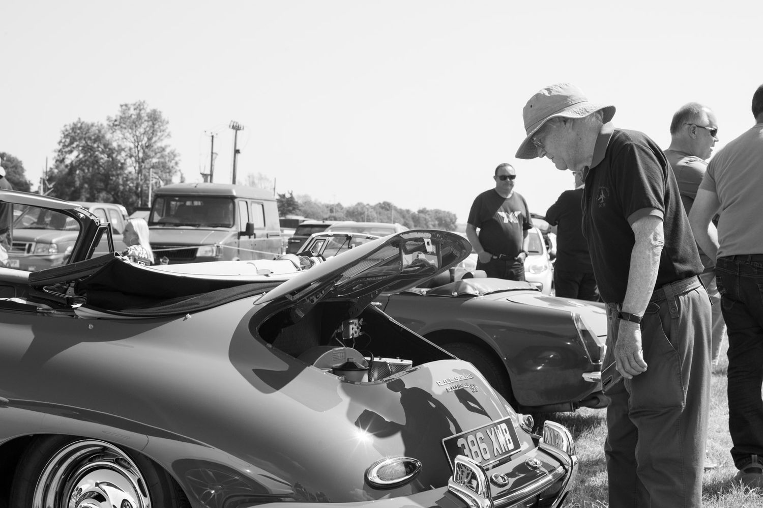 Classic cars lined up at an outdoor auto show with spectators admiring the vintage vehicles.