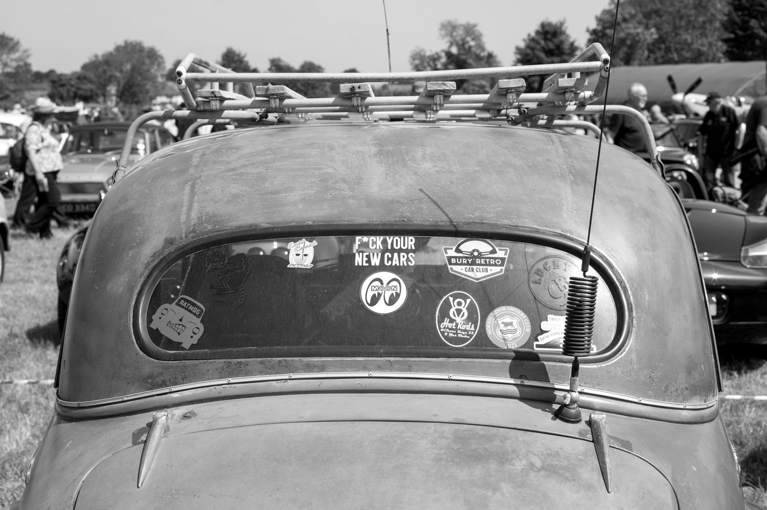 A series of vintage cars with windshield stickers parked in a row at a classic car show.