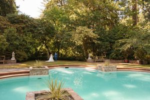 A curved swimming pool surrounded by stone walls and lush trees in an elegant backyard setting at dusk.