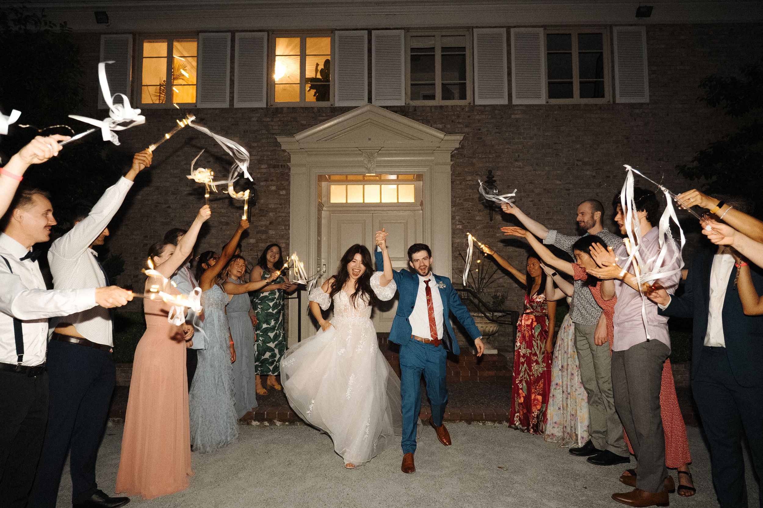 Wedding guests form a line and dance together at an evening reception with warm lighting and festive energy.
