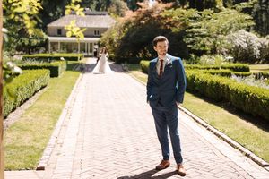 Wedding couple poses together in a lush garden setting with brick pathways and manicured hedges.