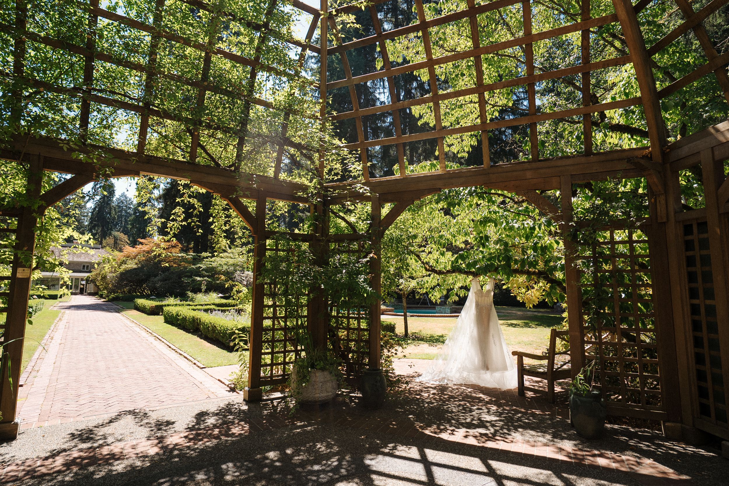 Panoramic view of a peaceful garden walkway with wooden railings surrounded by lush green trees and foliage.