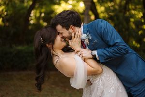 A romantic couple shares an intimate kiss outdoors in a sunlit natural setting with trees in the background.