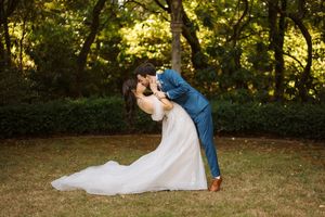 A romantic couple in wedding attire share a dramatic dip pose on a lush lawn during golden hour.
