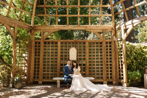 Wedding ceremony setup under a wooden pergola with lattice details and natural lighting.