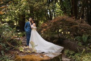 Couple in wedding attire walks through a scenic wooded forest path during an outdoor photoshoot.