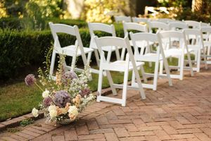 White folding chairs arranged on a brick patio with floral decorations for an outdoor wedding ceremony.