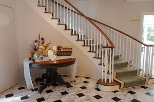 Interior panoramic view of a white staircase with wooden handrails and sage green carpet in a residential home.