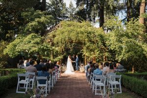 Wedding guests seated in white chairs during an outdoor garden ceremony at sunset.