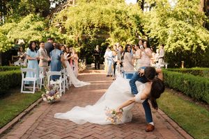 A couple performs a romantic dip on a garden path during an outdoor wedding celebration.