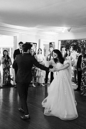 Wedding guests dancing and celebrating during a reception in an elegant white indoor venue.