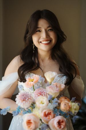 A bridal bouquet of peach and pink flowers with delicate blue accents in soft natural light.