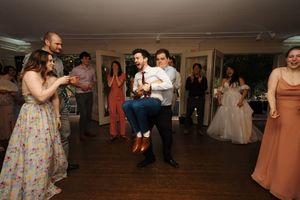 Wedding guests dance and celebrate together on a dimly lit dance floor at an indoor reception venue.