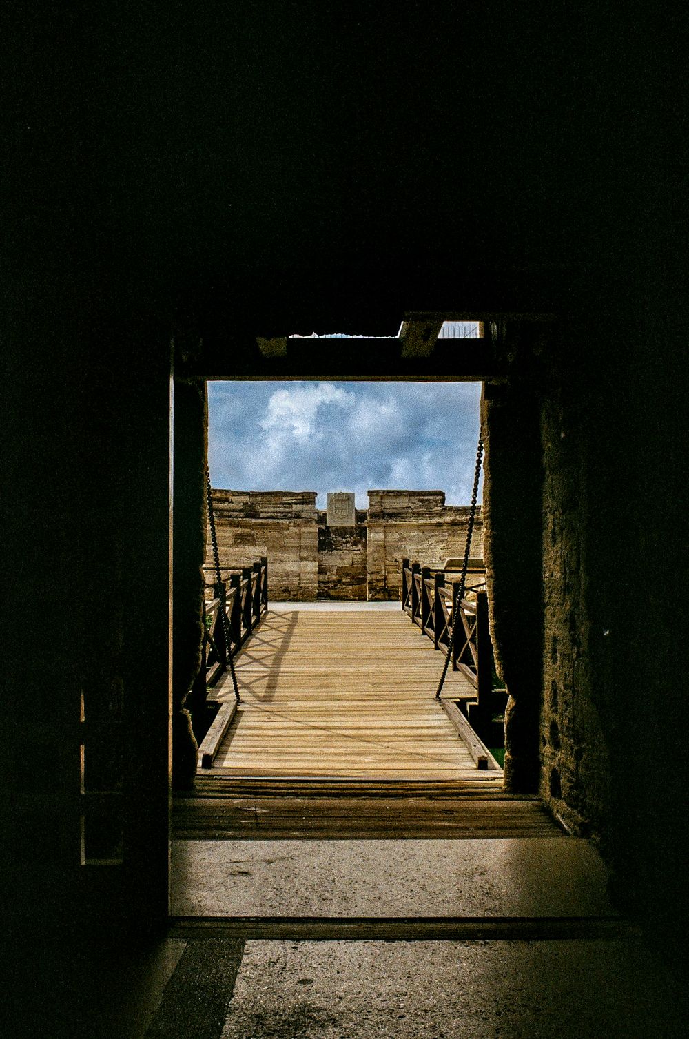 Dark tunnel opening to a wooden bridge walkway under bright blue skies.