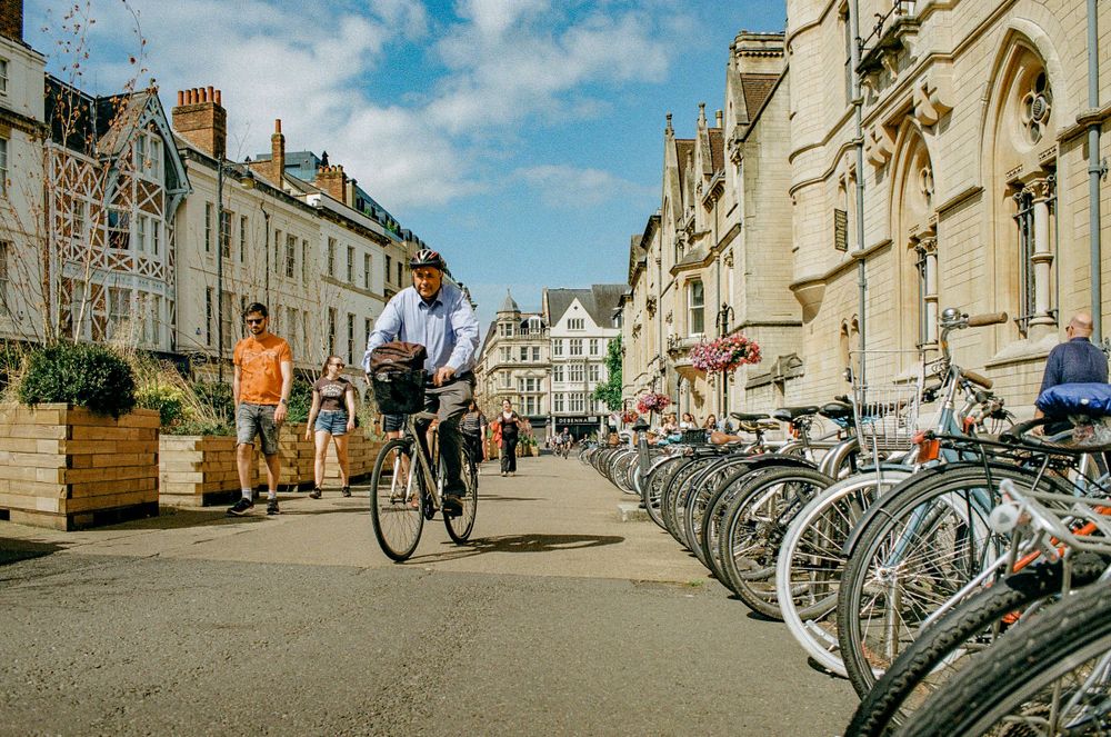 Person cycling past rows of parked bicycles along historic buildings in Oxford.