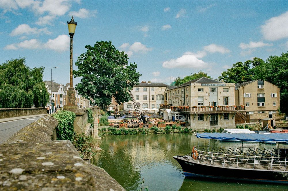 Peaceful riverside view in Bath with boats, lamp posts and stone buildings.