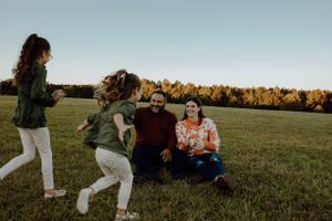A playful family moment captured in a grassy field with autumn trees in the background.