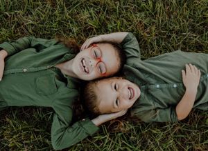 Two people laying on grass wearing matching olive green outfits while laughing together.