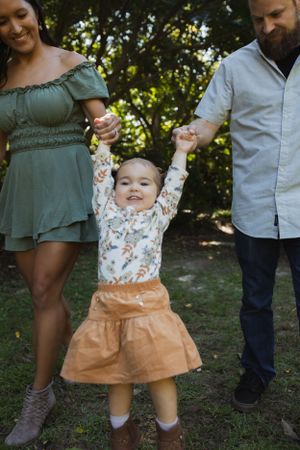A family enjoying a playful moment outdoors with their toddler in a floral outfit and orange skirt.