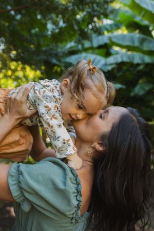A tender moment between parent and child outdoors with sunlit foliage in the background.