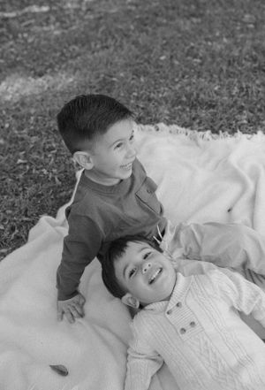 Two children laying on a blanket outdoors share a joyful moment in black and white photography.