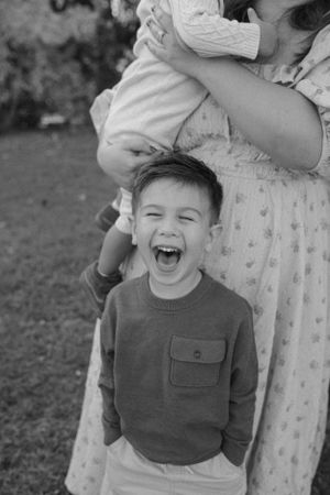 A child laughs exuberantly during a black and white family photo session outdoors.