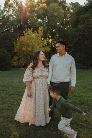 A family enjoys a playful moment in a park during golden hour as their child runs between them.