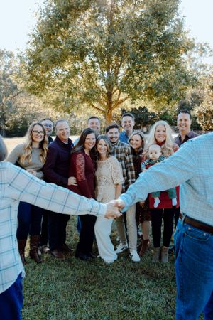Group photo with hands clasped in foreground under a large tree.