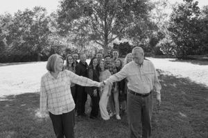 Group of people dancing in a line outdoors on a sunny day with trees in the background.